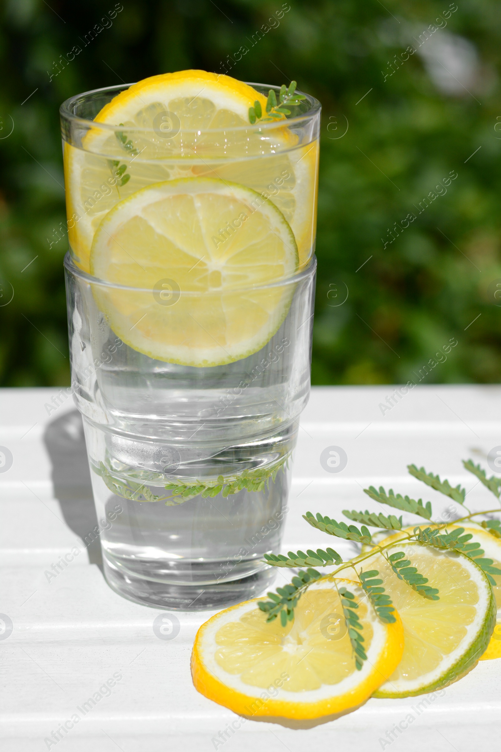 Photo of Delicious refreshing lemonade and pieces of citrus on white wooden table outdoors