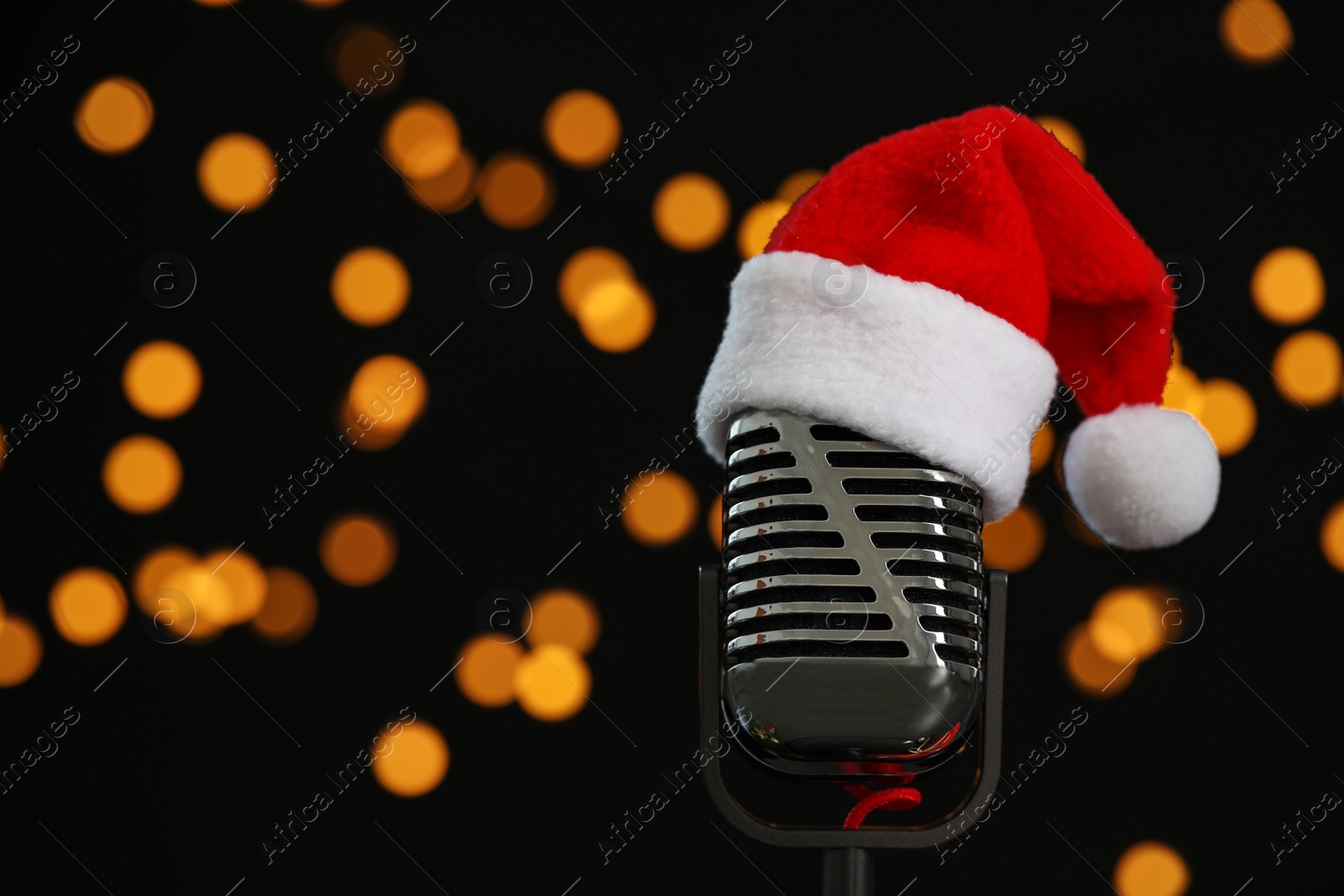 Photo of Microphone with Santa hat against blurred lights, space for text. Christmas music