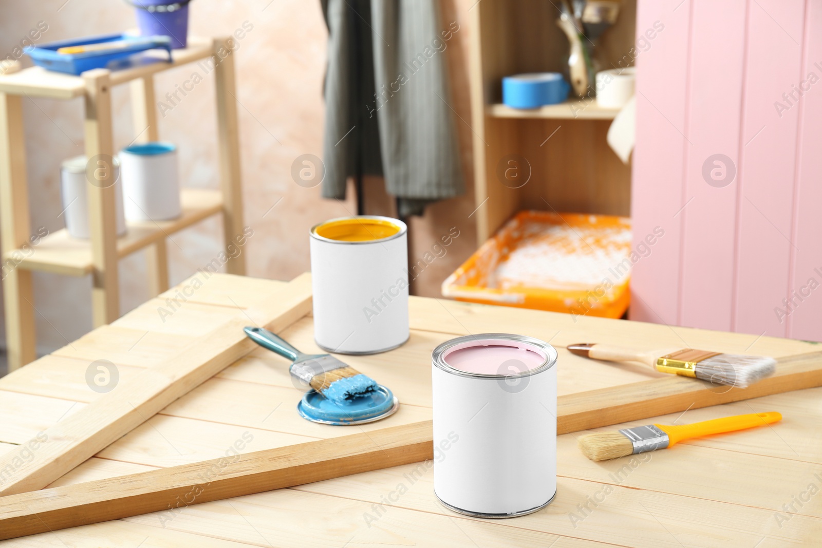 Photo of Cans of colorful paints and brushes on wooden table indoors