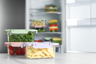 Photo of Containers with different frozen vegetables on white marble table near open refrigerator