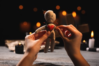 Photo of Woman stabbing voodoo doll with pin at wooden table indoors, closeup