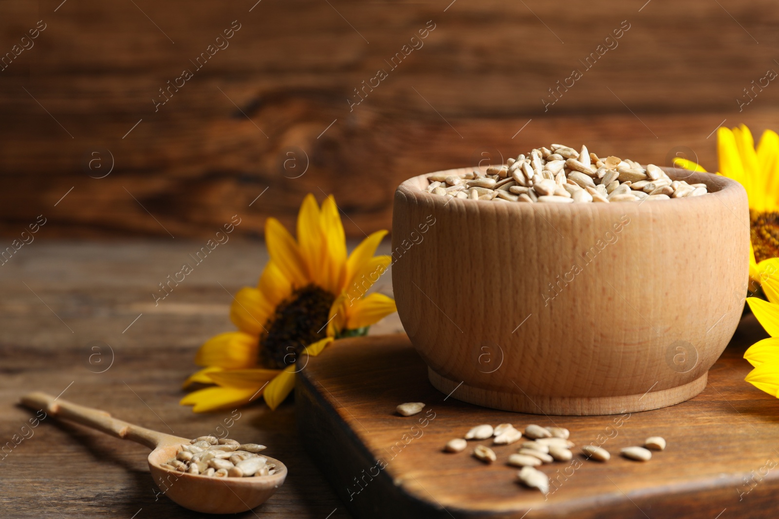 Photo of Raw peeled sunflower seeds and flowers on wooden table. Space for text