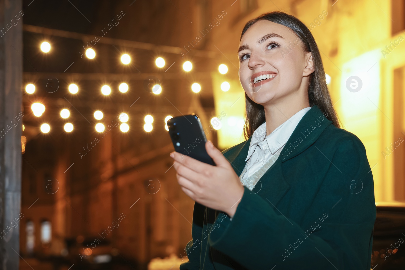 Photo of Smiling woman using smartphone on night city street. Space for text