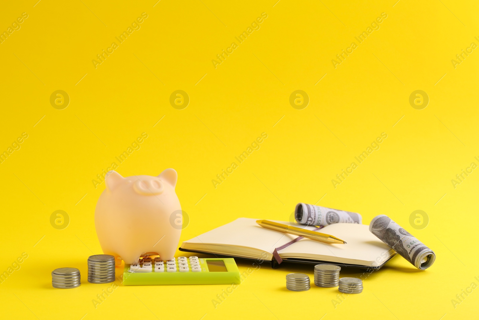 Photo of Financial savings. Piggy bank, money, calculator and stationery on yellow background