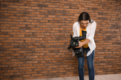 Operator with professional video camera near brick wall, space for text