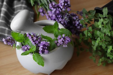 Mortar with fresh lavender flowers, mint and pestle on wooden table, closeup