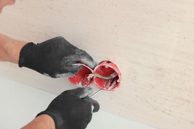 Photo of Electrician with screwdriver repairing power socket indoors, closeup. Space for text