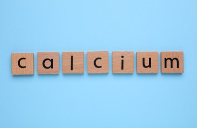 Photo of Word Calcium made of wooden cubes with letters on turquoise background, top view