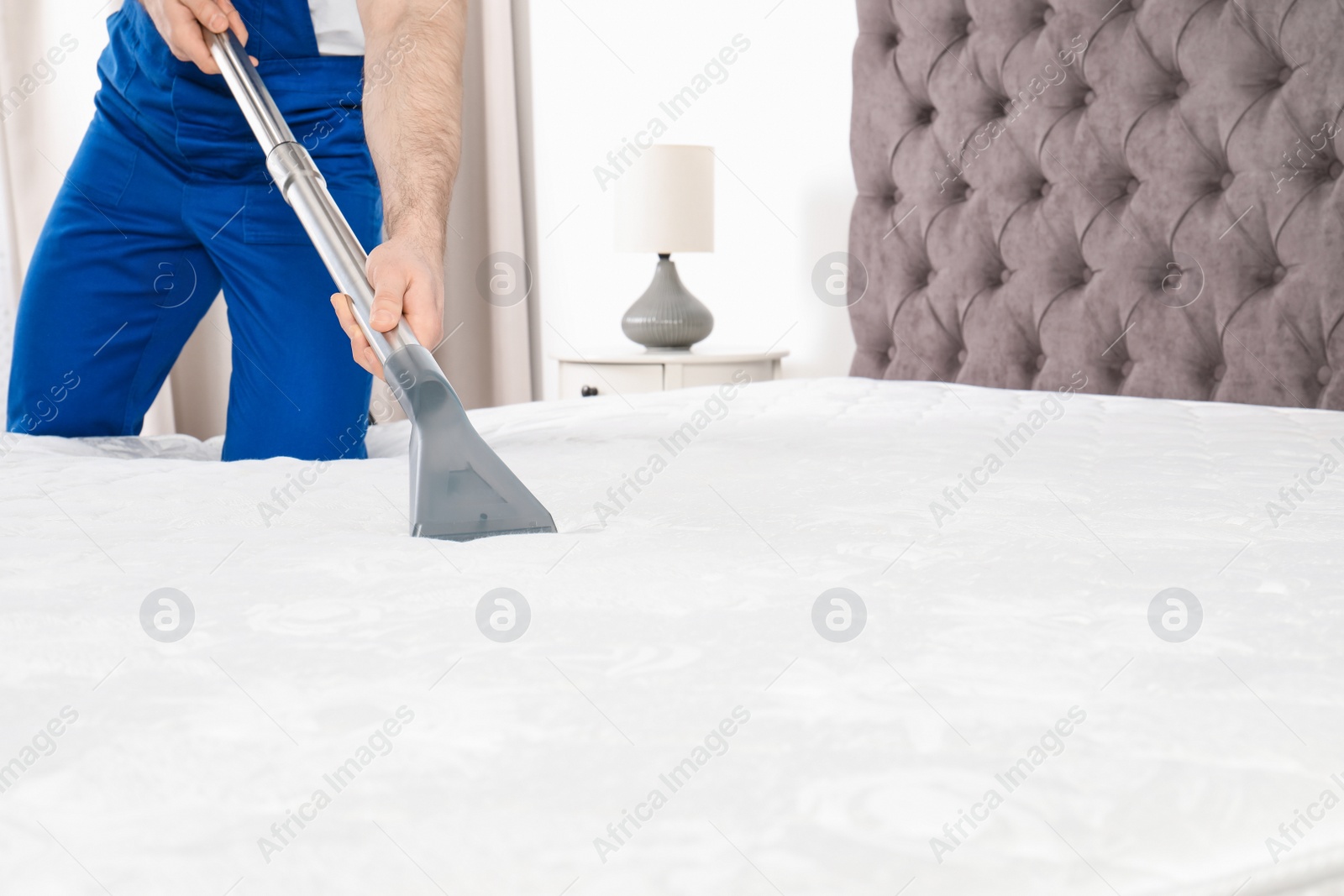 Photo of Man disinfecting mattress with vacuum cleaner, closeup. Space for text