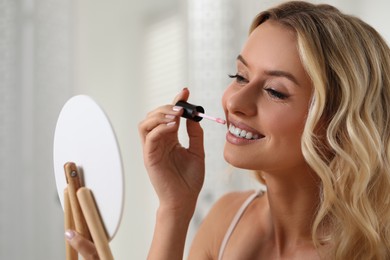 Beautiful makeup. Smiling woman with mirror applying liquid lipstick indoors