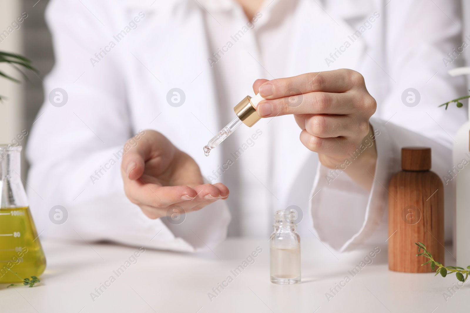 Photo of Dermatologist testing essential oil at white table indoors, selective focus