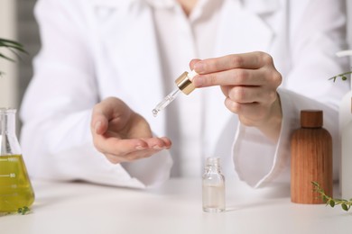 Photo of Dermatologist testing essential oil at white table indoors, selective focus