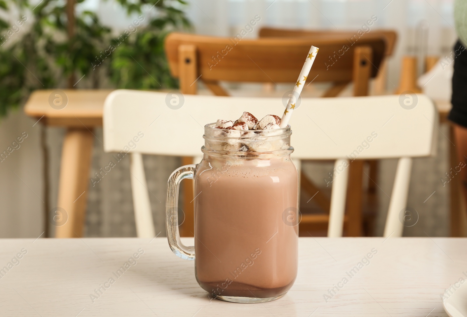 Photo of Delicious cocoa drink with marshmallows in mason jar on light table