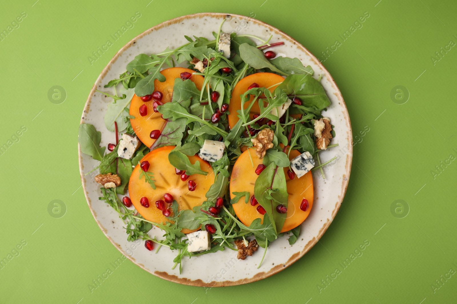 Photo of Tasty salad with persimmon, blue cheese and walnuts served on light green background, top view