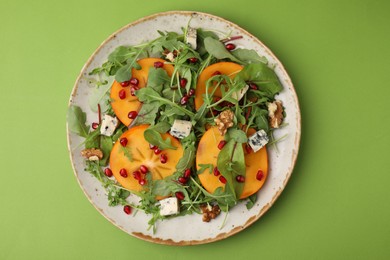 Tasty salad with persimmon, blue cheese and walnuts served on light green background, top view