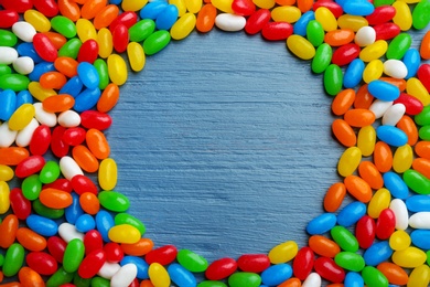 Photo of Frame made of colorful jelly beans on blue wooden background, flat lay. Space for text