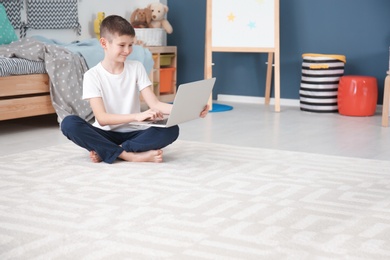 Happy boy with laptop sitting on cozy carpet at home