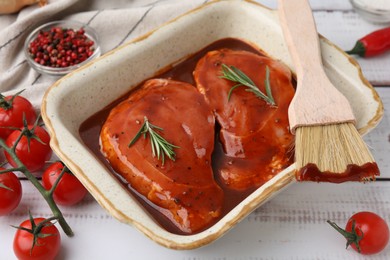 Photo of Raw marinated meat, rosemary and basting brush on white wooden table, closeup