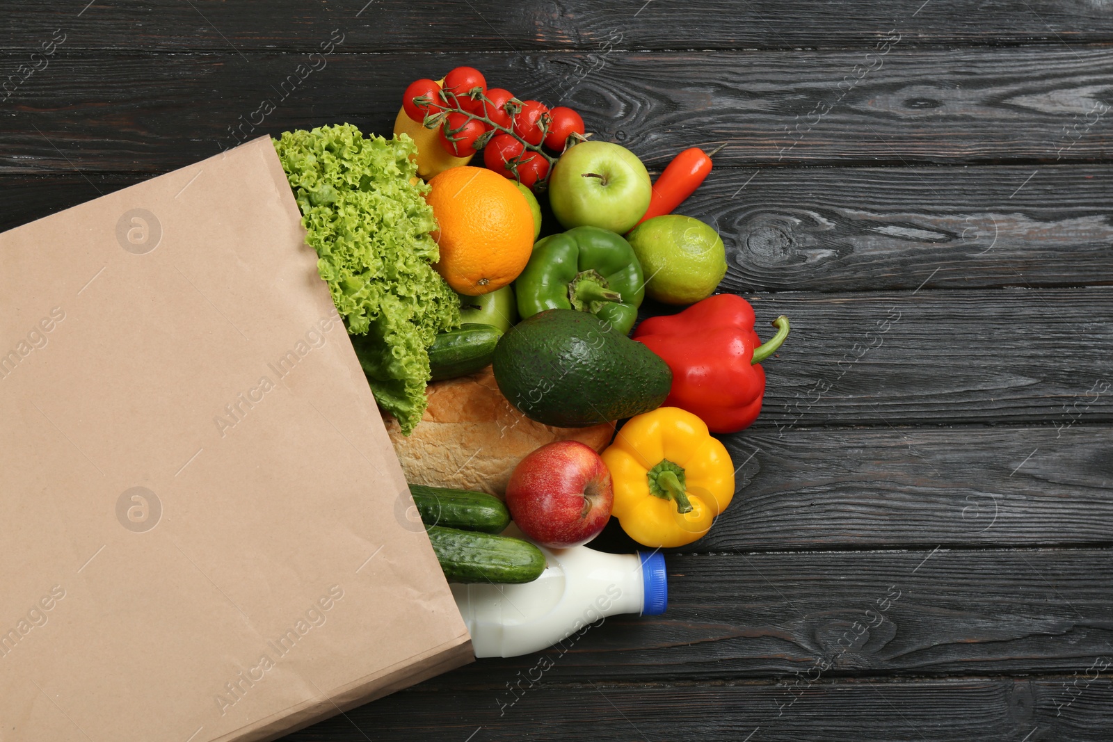 Photo of Overturned paper bag and groceries on black wooden background, top view