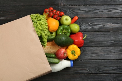 Overturned paper bag and groceries on black wooden background, top view