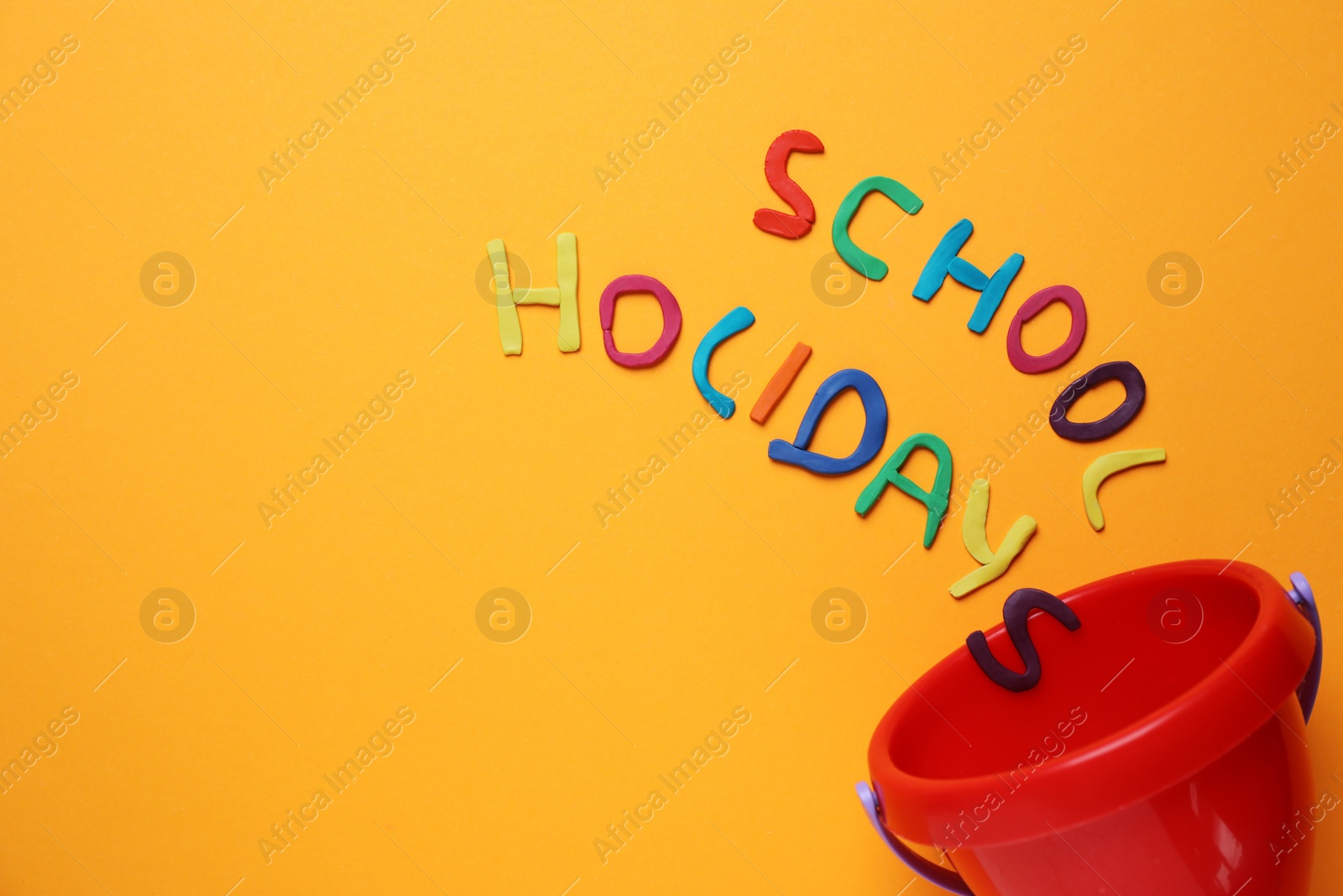 Photo of Phrase School Holidays made of modeling clay and plastic bucket on orange background, top view