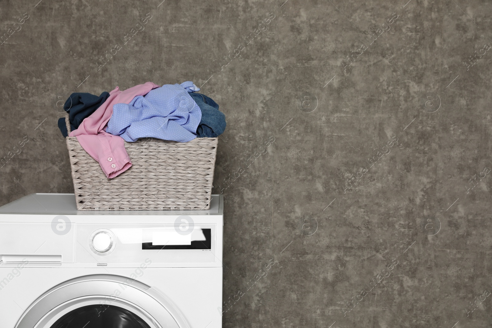 Photo of Wicker laundry basket full of dirty clothes on washing machine near color wall. Space for text