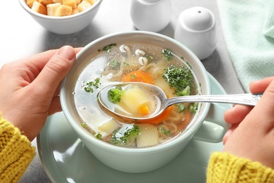 Woman eating fresh homemade vegetable soup at table, closeup