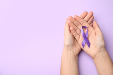 Photo of Woman holding purple ribbon on lilac background, top view with space for text. Domestic violence awareness