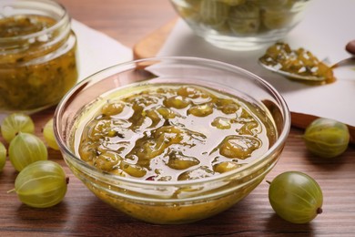 Bowl of delicious gooseberry jam and fresh berries on wooden table, closeup