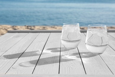 Photo of Wooden table with glasses of refreshing drink on hot summer day outdoors, space for text