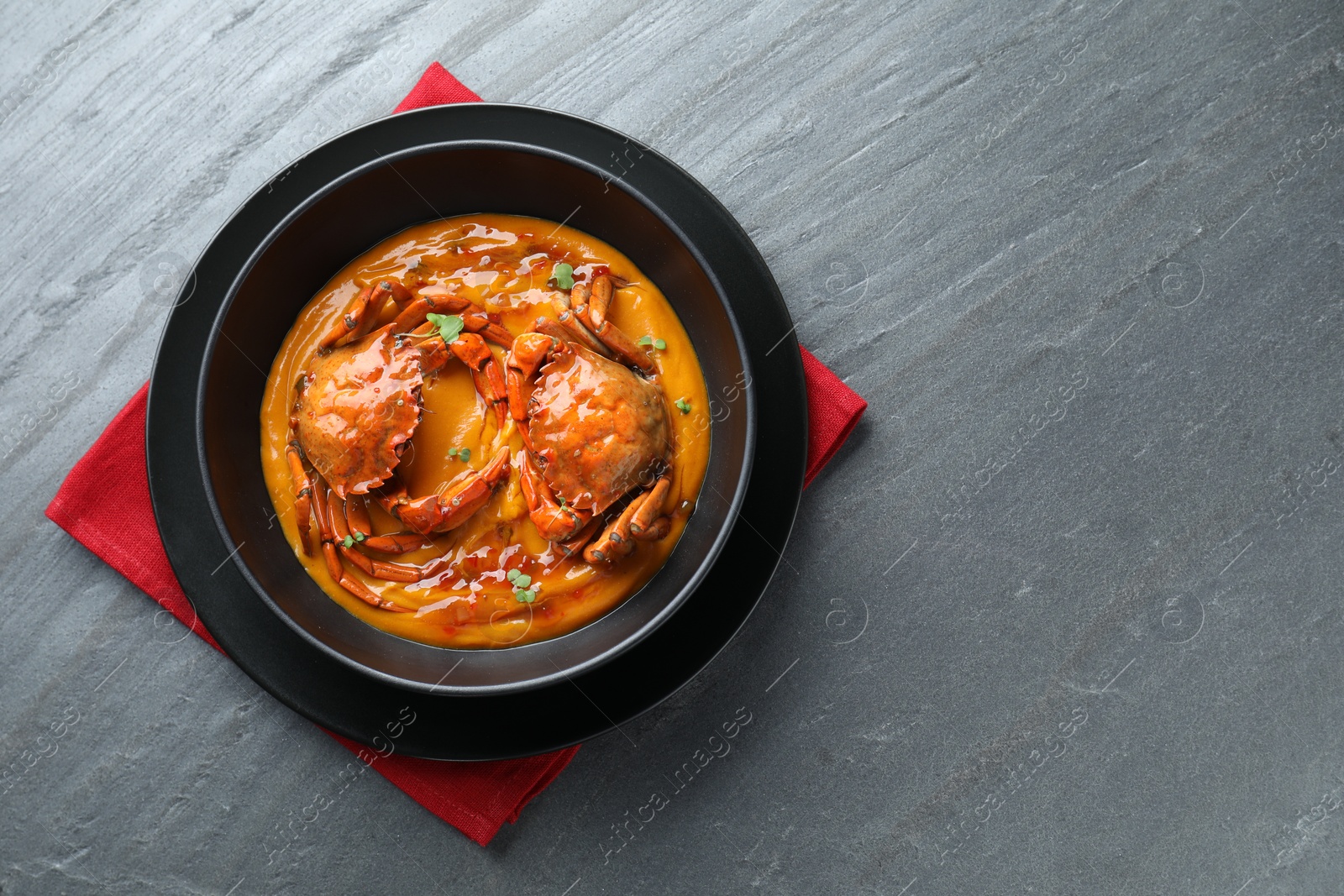 Photo of Delicious boiled crabs with sauce in bowl on grey textured table, top view. Space for text