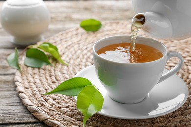 Photo of Pouring green tea into white cup with saucer on table, closeup