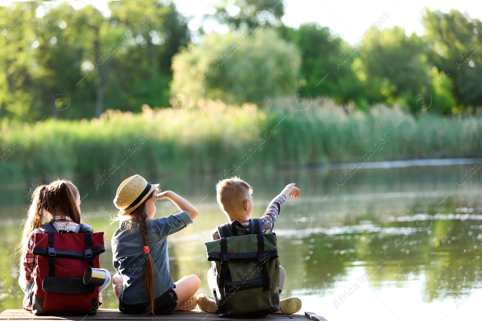 Photo of Little children sitting on wooden pier. Summer camp