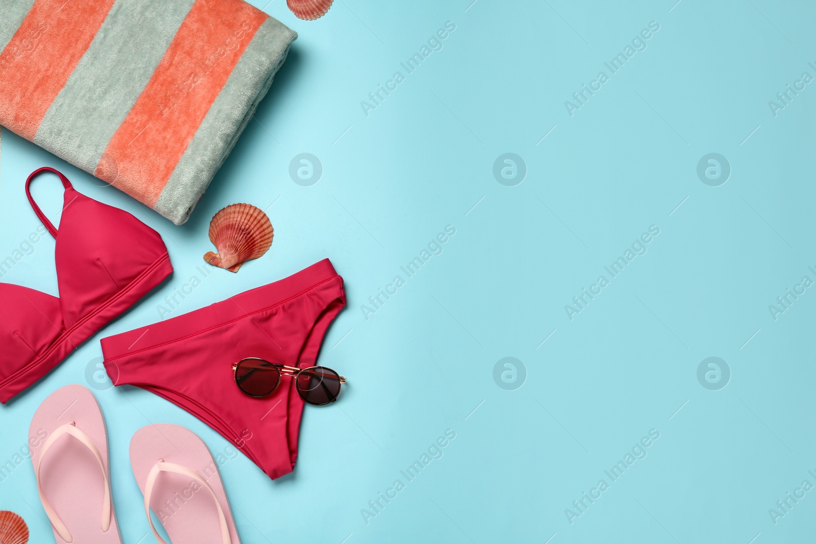 Photo of Beach towel, swimsuit, flip flops and sunglasses on light blue background, flat lay. Space for text