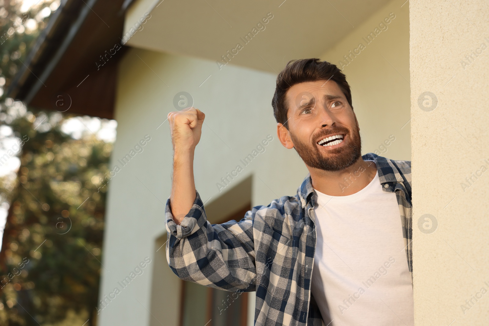 Photo of Angry man showing fist near house, low angle view. Annoying neighbour