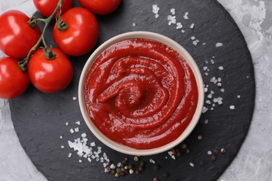 Organic ketchup in bowl, fresh tomatoes and spices on grey textured table, top view. Tomato sauce