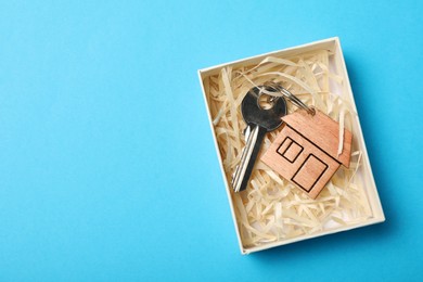 Key with trinket in shape of house on light blue background, top view and space for text. Housewarming party