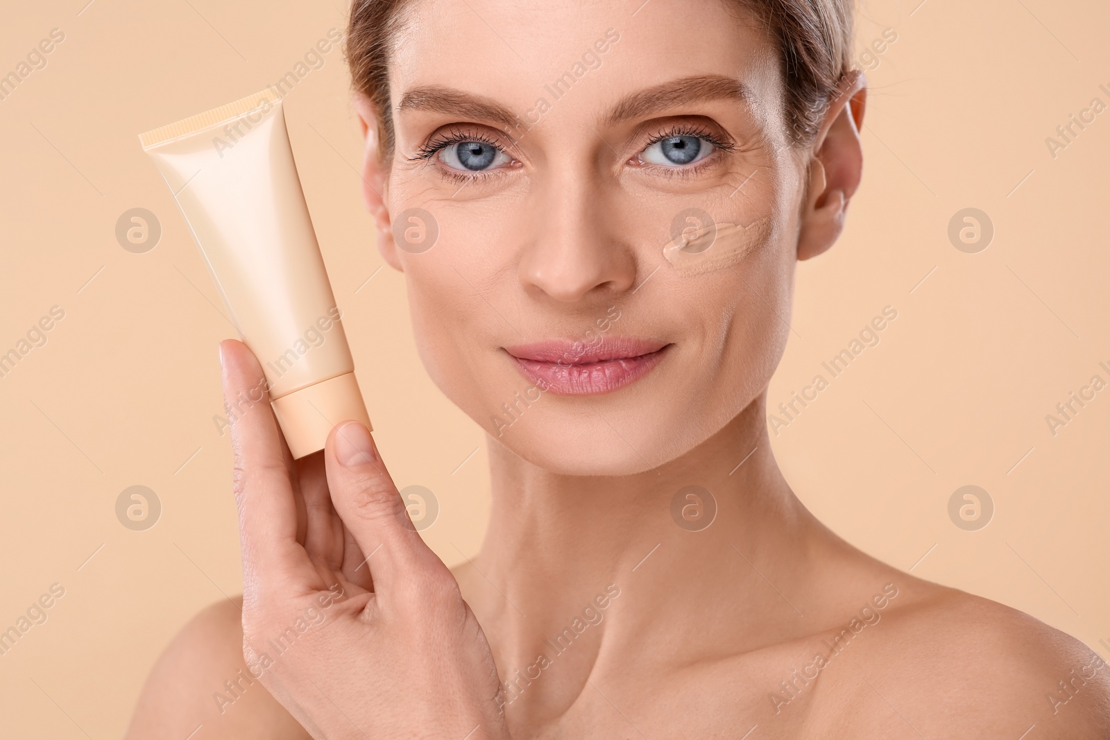 Photo of Woman holding tube of foundation on beige background