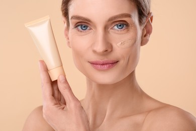 Woman holding tube of foundation on beige background