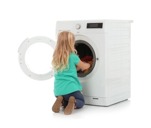 Photo of Cute little girl looking into washing machine with laundry on white background