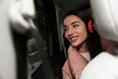 Photo of Beautiful young woman listening to music with headphones in public transport. Space for text