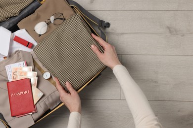 Photo of Woman packing suitcase on wooden floor, top view with space for text. Business trip planning