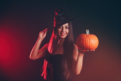 Photo of Young woman wearing witch costume with pumpkin on dark  background. Halloween party