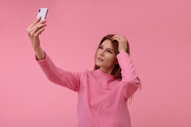 Beautiful woman taking selfie on pink background