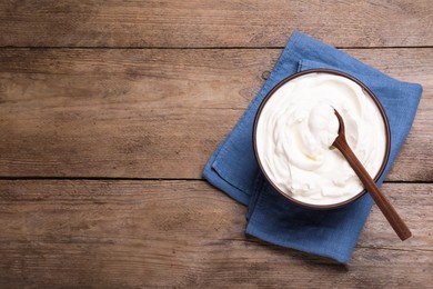 Top view of clay bowl with sour cream and spoon on wooden table, space for text