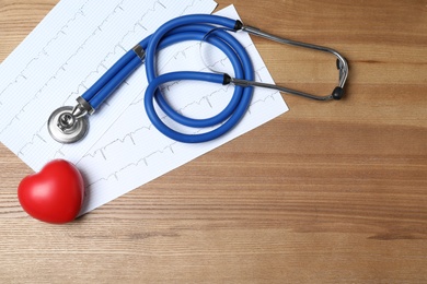 Stethoscope with red heart and cardiogram on wooden background, flat lay. Space for text