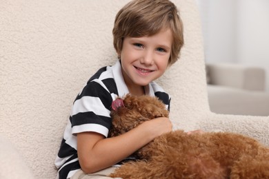 Photo of Little child with cute puppy in armchair indoors. Lovely pet