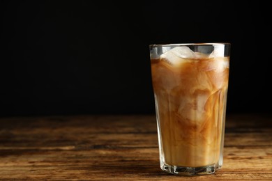 Photo of Glass of coffee with milk and ice cubes on wooden table. Space for text