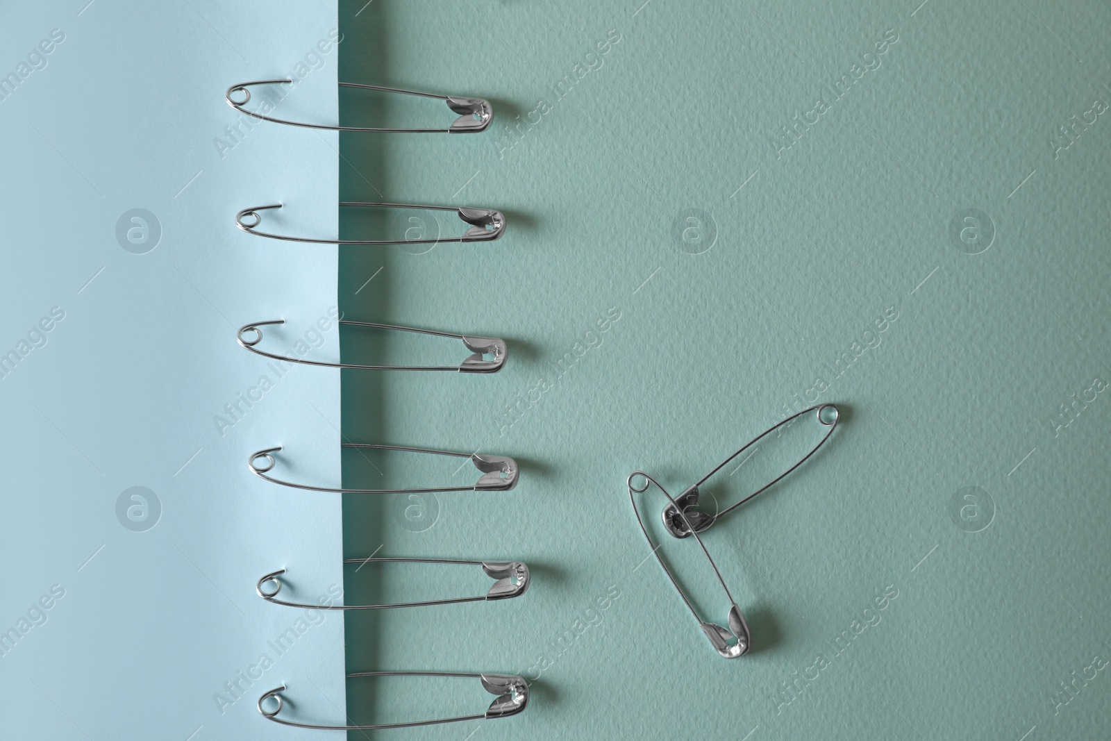 Photo of Many safety pins on light blue paper, flat lay. Space for text