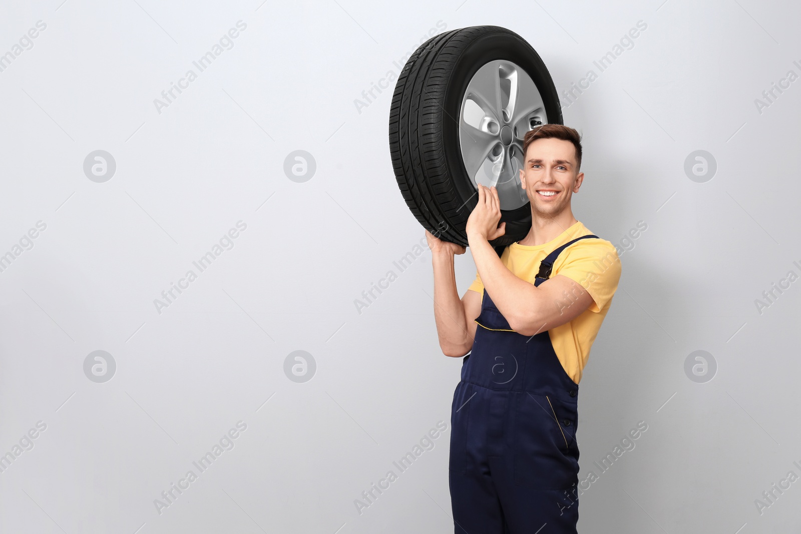 Photo of Male mechanic with car tire on light background